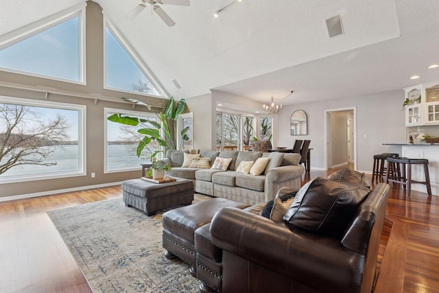 living area with ceiling fan with notable chandelier, high vaulted ceiling, baseboards, and wood finished floors