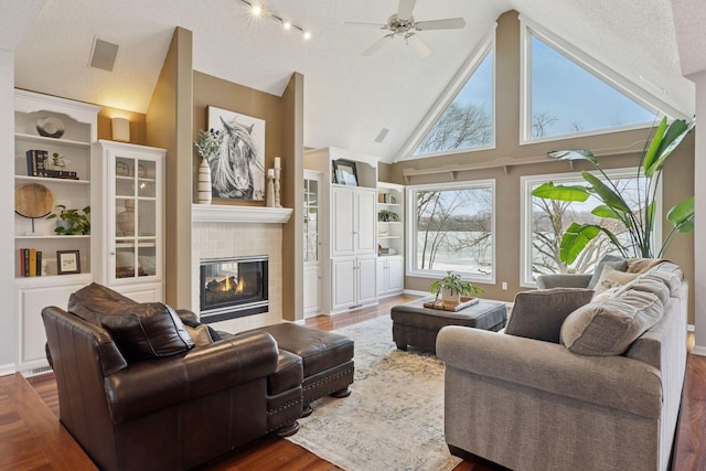 living area featuring ceiling fan, a tiled fireplace, high vaulted ceiling, wood finished floors, and a textured ceiling