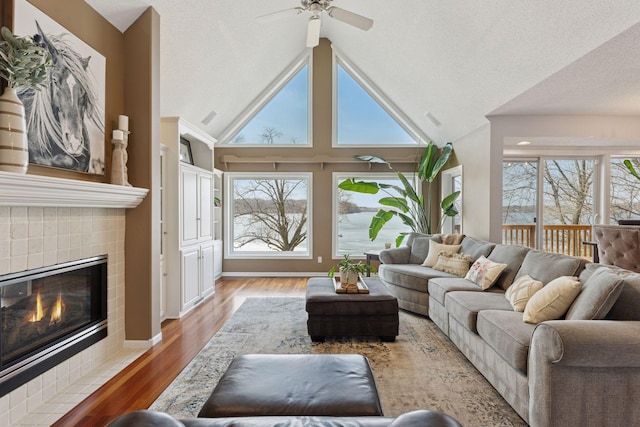 living area with visible vents, high vaulted ceiling, a ceiling fan, a tiled fireplace, and wood finished floors