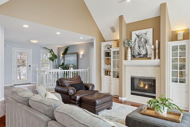 living area with wood finished floors, baseboards, lofted ceiling, recessed lighting, and a tile fireplace