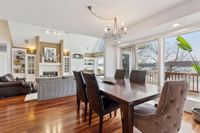 dining space with vaulted ceiling, a glass covered fireplace, wood finished floors, a notable chandelier, and a textured ceiling