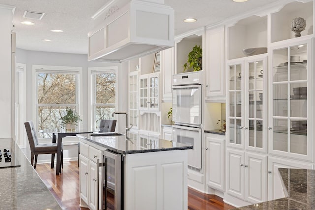 kitchen featuring wine cooler, white cabinets, double oven, and a sink