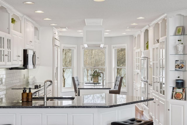 kitchen featuring dark stone countertops, a sink, decorative backsplash, white cabinets, and glass insert cabinets