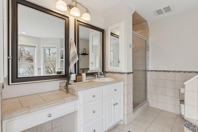 bathroom featuring visible vents, vanity, a stall shower, tile patterned floors, and tile walls