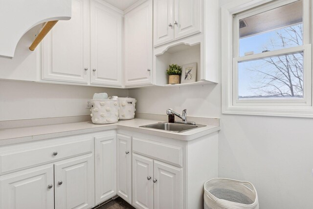 kitchen with white cabinetry, light countertops, open shelves, and a sink