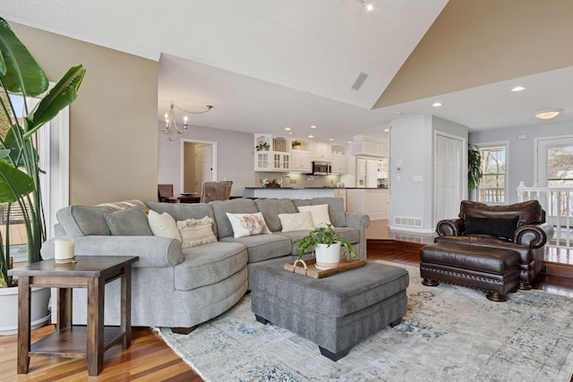 living area with recessed lighting, wood finished floors, high vaulted ceiling, and a chandelier