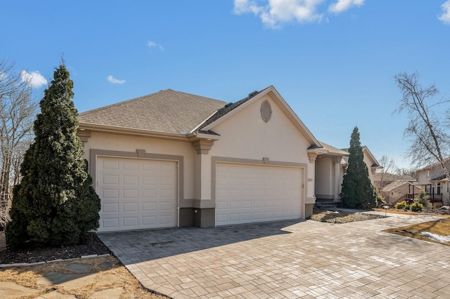 view of front of house featuring stucco siding, decorative driveway, a garage, and roof with shingles