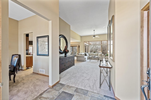 entrance foyer featuring visible vents, stone finish flooring, baseboards, carpet flooring, and a ceiling fan