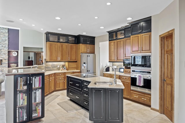 kitchen featuring a sink, glass insert cabinets, a center island with sink, appliances with stainless steel finishes, and dark cabinets