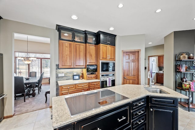 kitchen featuring a kitchen island with sink, built in microwave, a sink, oven, and black electric cooktop