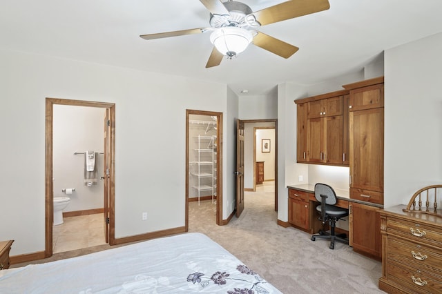 bedroom with baseboards, built in desk, ensuite bathroom, light carpet, and a walk in closet