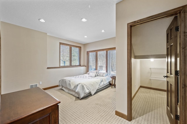 bedroom featuring a textured ceiling, light colored carpet, visible vents, and baseboards