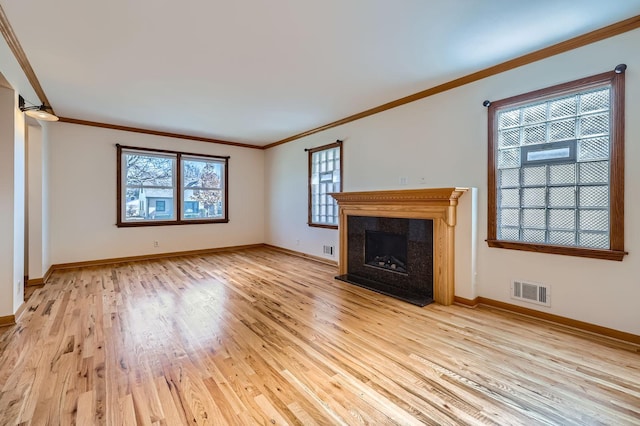 unfurnished living room featuring baseboards, visible vents, a high end fireplace, ornamental molding, and light wood-type flooring