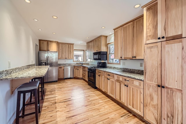 kitchen featuring light stone countertops, a breakfast bar area, light wood-style flooring, black appliances, and a sink