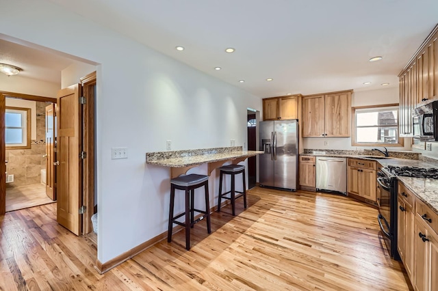 kitchen with light wood-type flooring, a breakfast bar, a sink, light stone counters, and appliances with stainless steel finishes