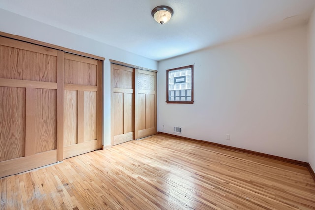 unfurnished bedroom featuring visible vents, baseboards, light wood-style floors, and multiple closets