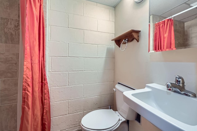 full bathroom featuring a sink, a shower with curtain, toilet, and concrete block wall