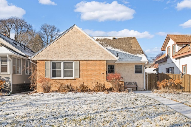 snow covered back of property with brick siding, roof with shingles, and fence