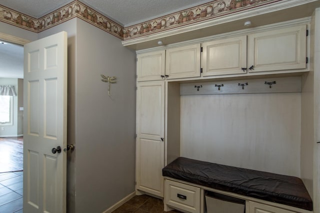 mudroom with dark tile patterned flooring, baseboards, and a textured ceiling