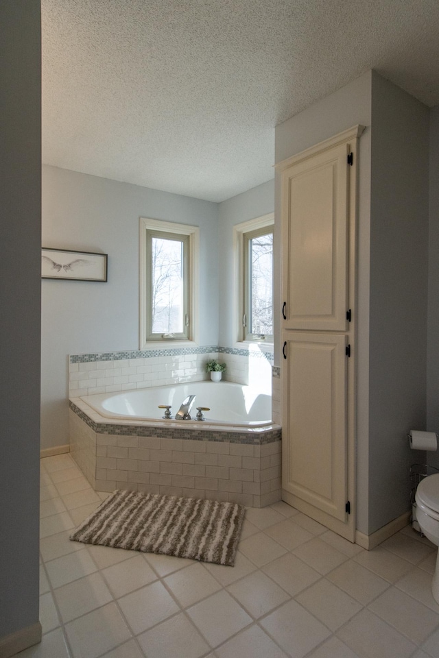 full bathroom with tile patterned flooring, baseboards, toilet, a garden tub, and a textured ceiling