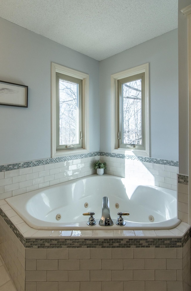 full bath with plenty of natural light, a textured ceiling, and a tub with jets
