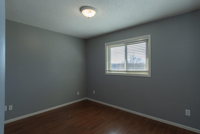spare room with a textured ceiling, baseboards, and dark wood-style flooring
