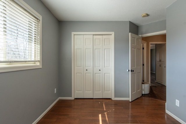 unfurnished bedroom with dark wood-style floors, a closet, and baseboards