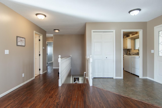 corridor with an upstairs landing, washing machine and dryer, dark wood finished floors, and baseboards