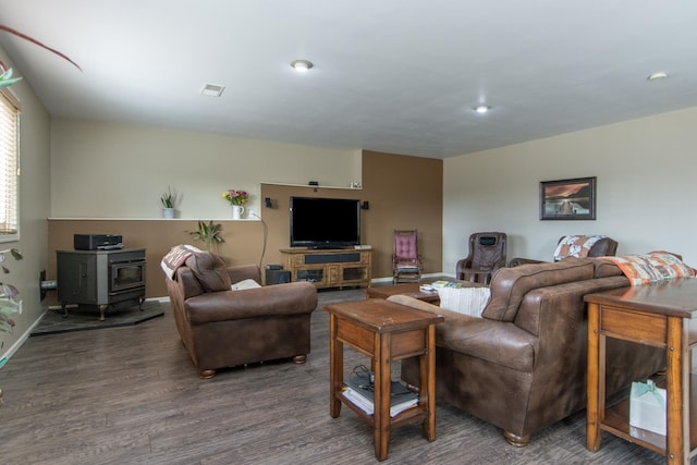 living room featuring a wood stove, wood finished floors, visible vents, and baseboards