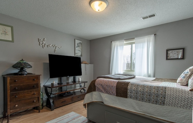 bedroom featuring visible vents, light wood-style flooring, and a textured ceiling