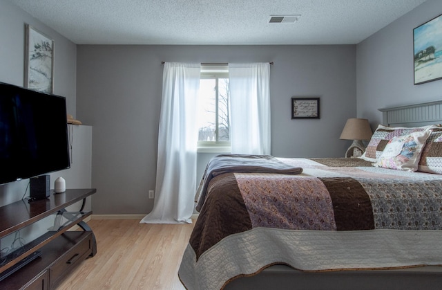 bedroom with light wood finished floors, visible vents, a textured ceiling, and baseboards
