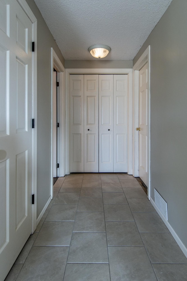 corridor featuring light tile patterned floors, baseboards, visible vents, and a textured ceiling