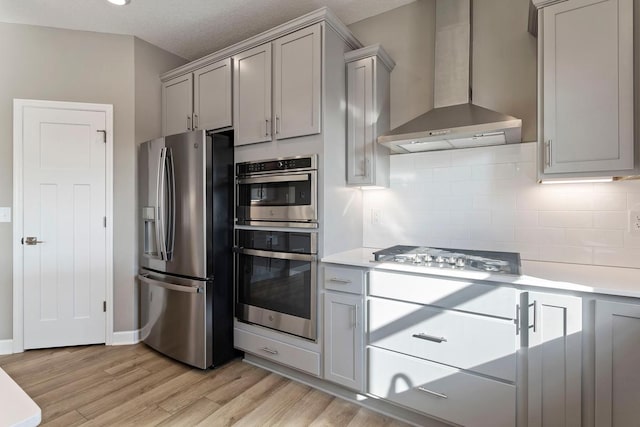 kitchen featuring wall chimney range hood, light wood-type flooring, gray cabinets, and stainless steel appliances