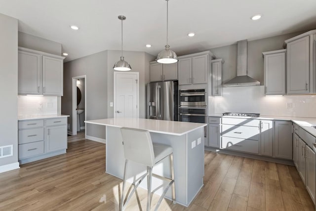 kitchen with appliances with stainless steel finishes, gray cabinets, and wall chimney range hood