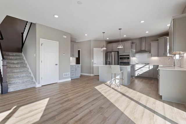 kitchen featuring visible vents, gray cabinetry, a kitchen island, stainless steel appliances, and wall chimney exhaust hood