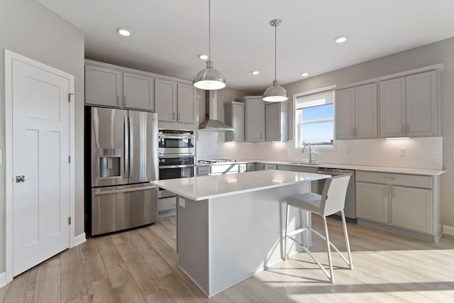 kitchen featuring a kitchen island, gray cabinets, a sink, stainless steel appliances, and wall chimney range hood