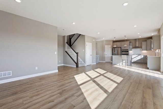 unfurnished living room featuring recessed lighting, light wood-style flooring, and stairs