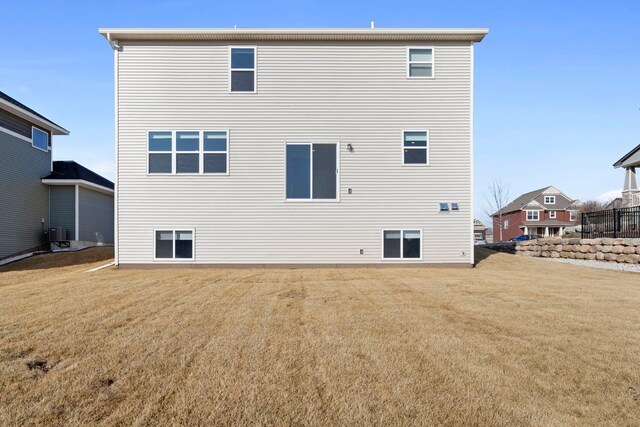 rear view of property with central AC unit and a lawn