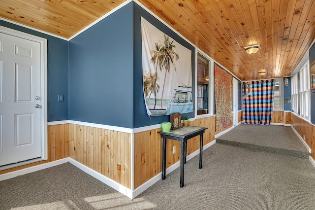 hallway with carpet floors, a wainscoted wall, baseboards, wooden ceiling, and wood walls