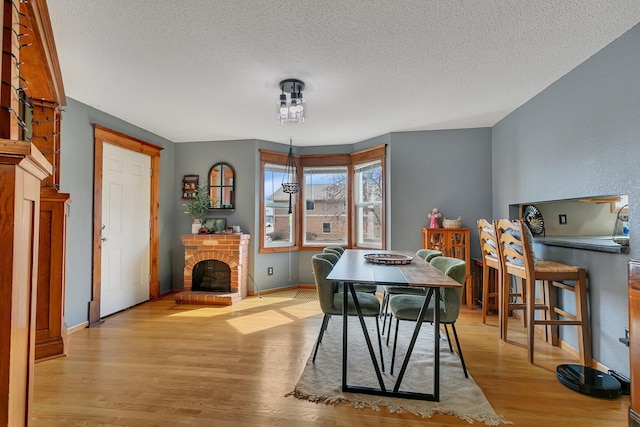 dining space with baseboards, a brick fireplace, a textured ceiling, and light wood-style flooring