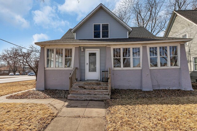 bungalow-style house with a shingled roof and stucco siding