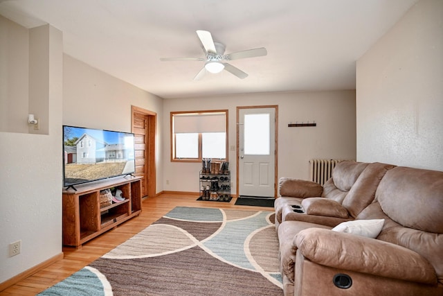 living area with light wood finished floors, baseboards, radiator heating unit, and a ceiling fan