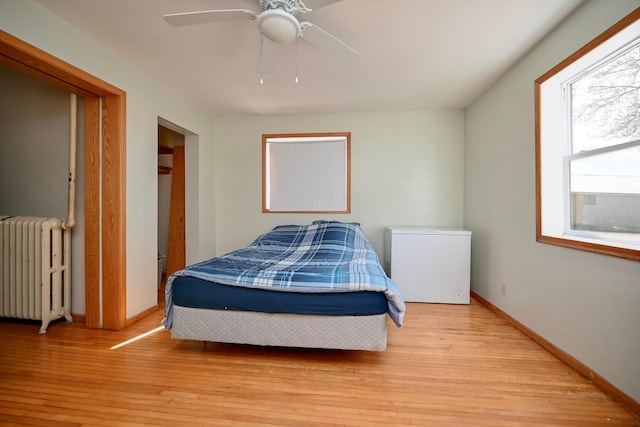 bedroom featuring radiator, baseboards, wood finished floors, refrigerator, and a ceiling fan