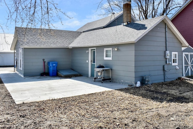 rear view of property featuring a patio, a chimney, and roof with shingles