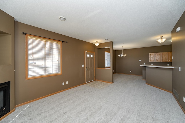 unfurnished living room featuring visible vents, baseboards, light carpet, a fireplace, and an inviting chandelier