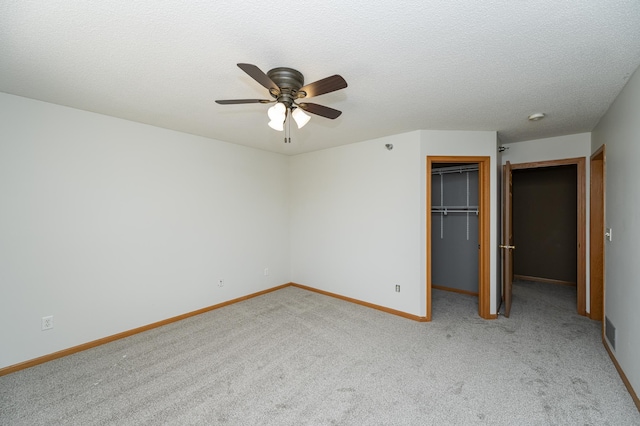 unfurnished bedroom featuring a textured ceiling, baseboards, visible vents, light carpet, and a walk in closet