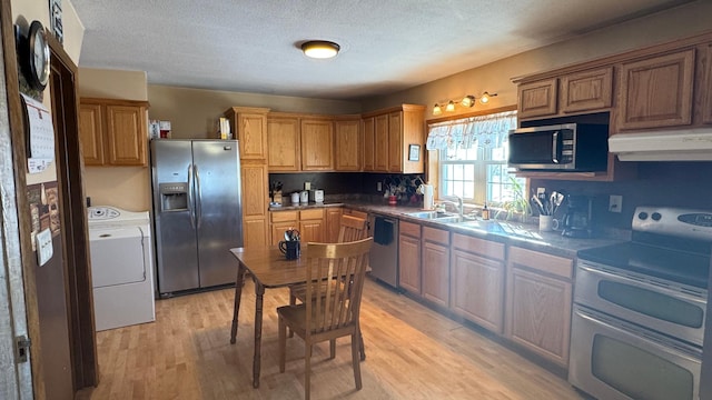 kitchen featuring light wood finished floors, washer / dryer, a sink, appliances with stainless steel finishes, and under cabinet range hood