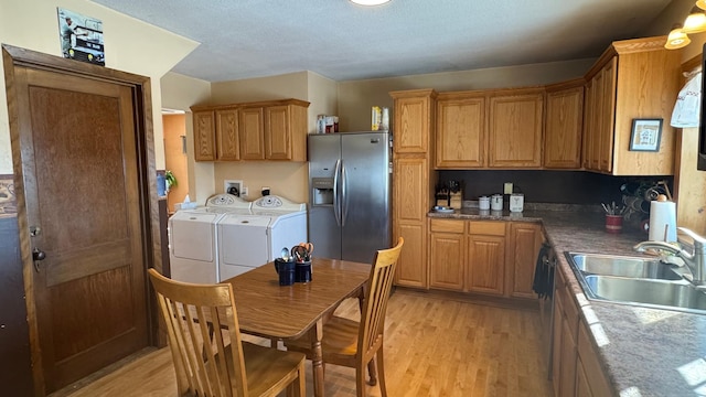 kitchen featuring stainless steel fridge with ice dispenser, a sink, light wood-style floors, washer and dryer, and brown cabinets