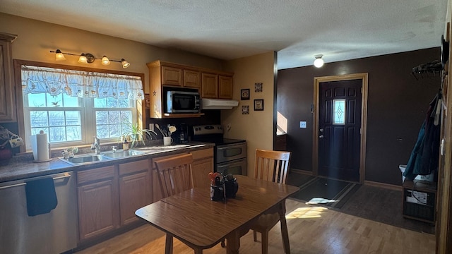 kitchen featuring a sink, under cabinet range hood, appliances with stainless steel finishes, dark countertops, and light wood-type flooring