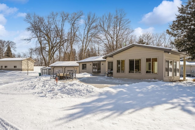 snow covered rear of property with a shed, a detached garage, and an outdoor structure